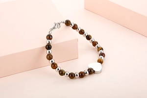Detail of brown tiger eye beads and silver heart pendant on a steel bracelet