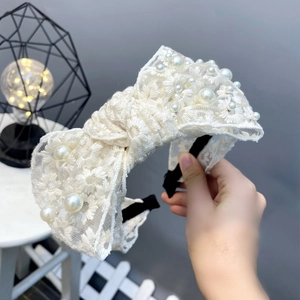 Detailed view of white lace headband featuring intricate floral embroidery and faux pearls