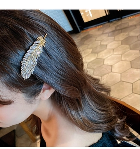 Detailed view of a gold feather hair clip with sparkling rhinestones on a female model