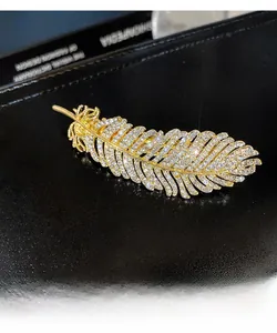 Close-up of golden feather hair clip featuring intricate diamond inlay on a black surface