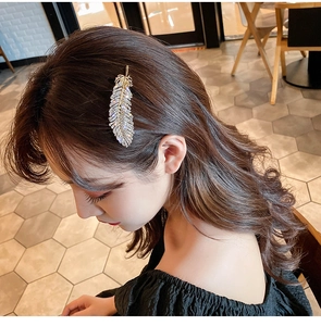 Detailed view of a glittering feather hair clip with rhinestones worn by a model