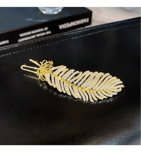 Detailed close-up of a golden feather hair clip with white pearls on a black leather background