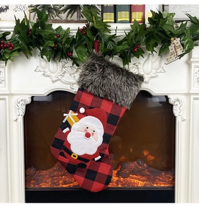Detail of red buffalo plaid Christmas stocking with Santa Claus applique hanging on fireplace