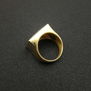 Detailed view of square gold-plated stainless steel ring on a black textured background