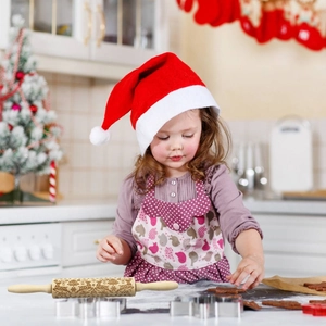 Young girl using Christmas elk embossed wooden rolling pin to make festive holiday cookies