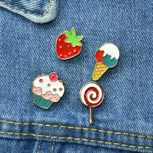 Close-up of strawberry, ice cream, and cupcake enamel pins on denim fabric background