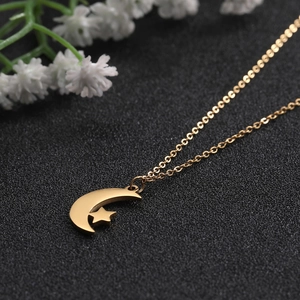 Close-up of a gold hollow moon and star pendant necklace on a textured black surface