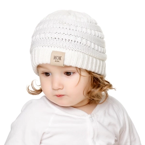 Close-up of white knitted baby hat featuring a brown leather patch and ribbed texture
