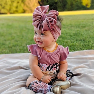 Infant girl velvet bow headband in dusty pink with matching floral outfit in sunlight