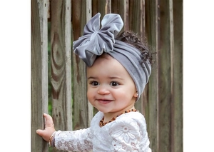 Close-up of a large grey velvet bow headband on a baby girl with outdoor wooden background