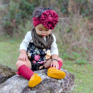 Outdoor shot of infant in floral romper with oversized burgundy flower headband and scarf