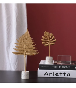 Detailed view of golden metal monstera and fern leaf sculptures with white terrazzo bases