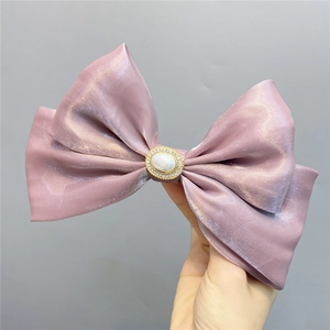 Macro shot of large purple satin double bow hair clip with central pearl and rhinestones