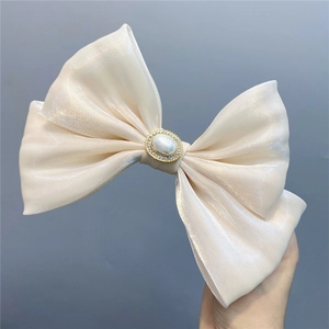 Close-up of a large ivory satin bow hair clip with central pearl and rhinestone accents