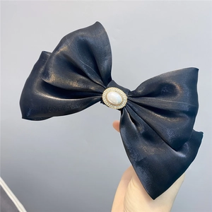 Close-up of double-layered black bow hair clip with central pearl and rhinestone trim