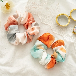 Detailed view of two gradient tie-dye hair scrunchies with elegant floral and lace props