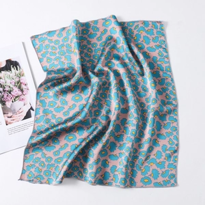 Detail of pink silk square scarf featuring blue floral patterns and smooth edges
