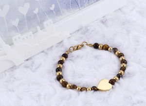 Detail of tiger eye stone bracelet with golden heart pendant on white plush surface