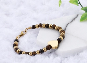 Close-up of tiger eye stone beads and gold heart pendant on a soft white plush surface