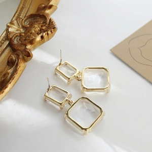 Close-up of golden geometric square drop earrings with clear artificial crystal detail