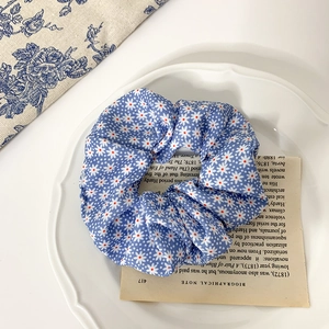 Gros plan d'un chouchou bleu à motifs marguerites sur papier décoratif et assiette blanche