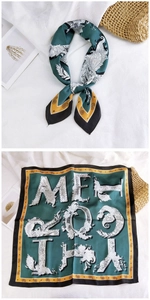 Close-up of silk-textured square scarf featuring dark green paisley patterns and artistic letters
