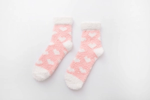 Detailed view of pink coral fleece mid-calf socks with white heart patterns and plush texture
