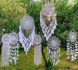 White bohemian dreamcatchers with crochet lace and feathers hanging against a green garden