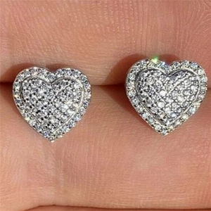 Macro detail of silver heart stud earrings featuring micro-pave cubic zirconia on a finger