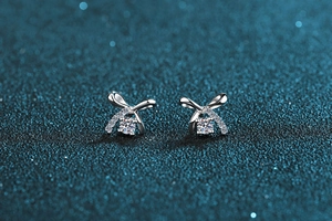 Macro detail of silver bow earrings with round moissanite and shimmering blue background