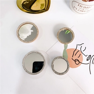 Detail of round rhinestone phone grips and makeup mirrors on a luxury tray background