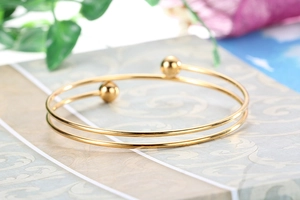 Detail of a minimalist gold double-layer open bangle with smooth spherical ends