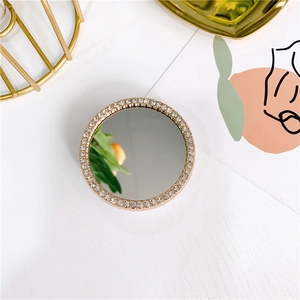 Detail of round gold makeup mirror with sparkling rhinestone border on white wood background