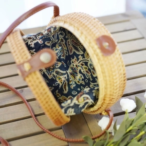 Detail view of round woven rattan bag with paisley lining and leather strap on wooden desk