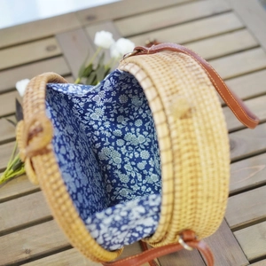 Detail of round rattan bag with blue floral lining and leather shoulder strap