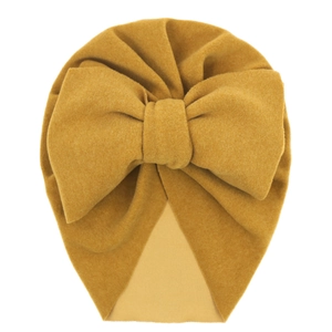 Detail of ginger yellow baby turban hat with oversized knit bow on a white background