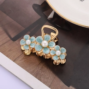 Pince à cheveux dorée avec fleurs en émail bleu et perles sur un magazine ouvert