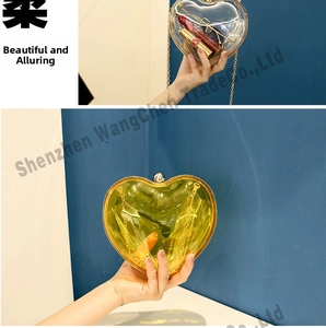 Macro detail of a heart-shaped acrylic evening bag with a gold chain strap and metal clasp