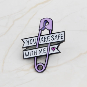 Detailaufnahme der lila Emaille-Brosche mit weißem Banner und You Are Safe With Me Spruch