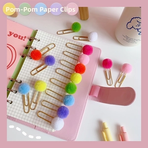 Detail showing colorful macaron pom-pom balls and golden metal paperclips on a desk