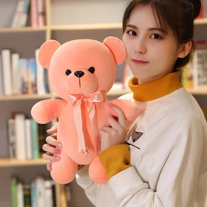 Pink plush teddy bear toy with ribbon bow held by a person in a cozy home setting