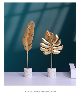 Detail of gold metal monstera and feather leaves on marble bases for home decor