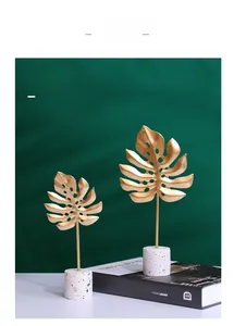 Detail of two gold metal monstera leaf sculptures on white marble bases