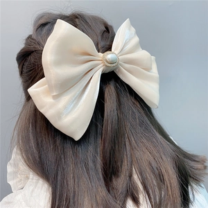 Detail of a large creamy white satin bow hair clip with central pearl and gold rhinestones