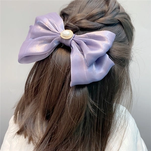 Detail view of a large purple silk bow hair clip with central pearl on a model's hair