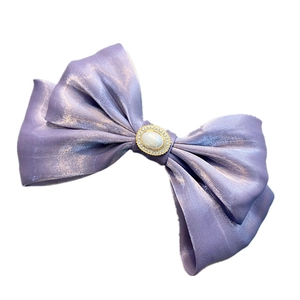 Close-up of a purple satin double bow hair clip with central pearls and small rhinestones