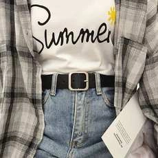 Detail of a black leather belt with silver square buckle on blue jeans and white summer tee