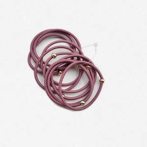 Dettaglio di elastici per capelli viola con perline dorate su sfondo bianco minimale