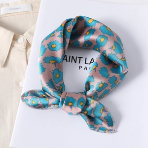 Detailed view of pink floral silk scarf tied in a knot on a white book and beige shirt