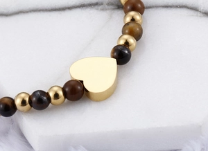 Macro detail of a golden heart pendant and brown tiger eye beads on a beaded bracelet
